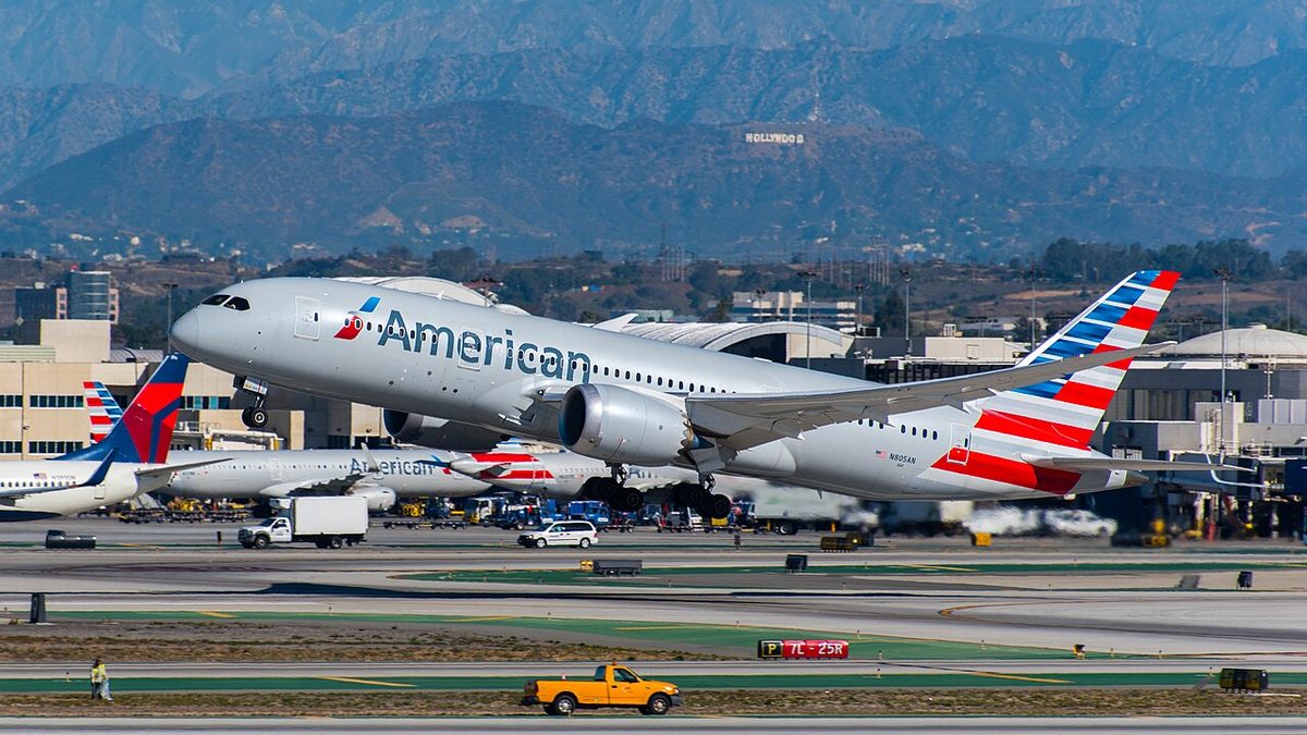 An American Airlines Boeing 787-8 Dreamliner lifting off from Los Angeles International Airport, with the Hollywood sign on the hills behind it