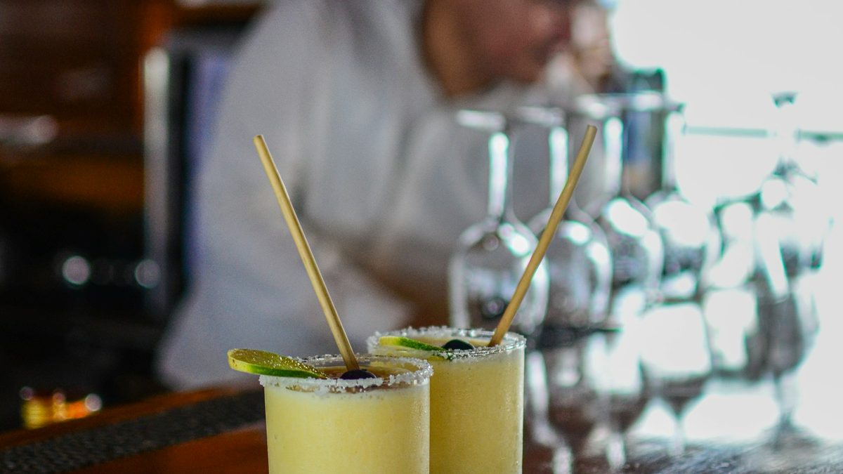 Two margarita cocktails with lime and salted rims on a wooden bar counter