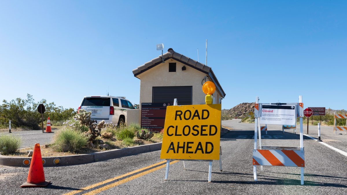 A Road Closed Ahead sign and barricade at a Joshua Tree National Park entrance, with a US Park Ranger vehicle parked behind it