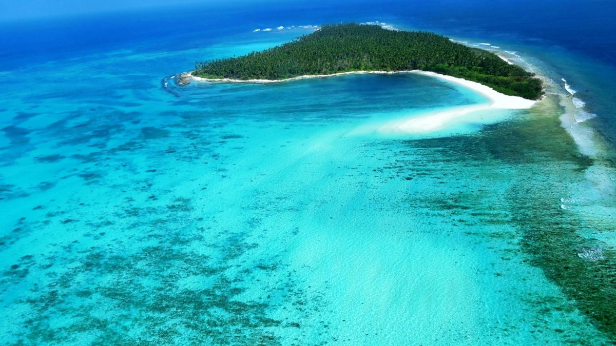 A coral atoll ringed by a shallow turquoise lagoon and reef flat, seen from the air