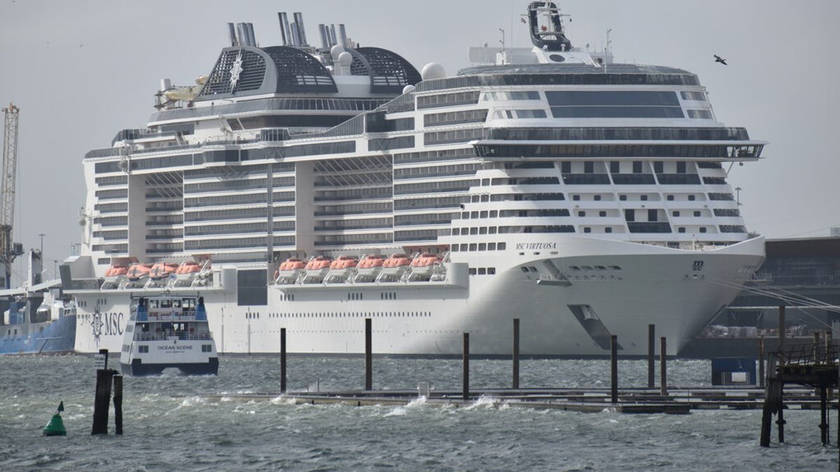 A large cruise ship berthed at a cruise terminal in Southampton, England, with a small ferry passing in front