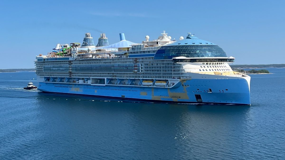 Icon of the Seas, a large Royal Caribbean cruise ship, under way at sea with a tug boat alongside