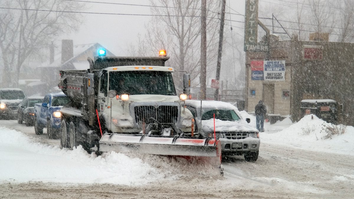 A snowplough clearing a Colorado street past a tavern during heavy falling snow