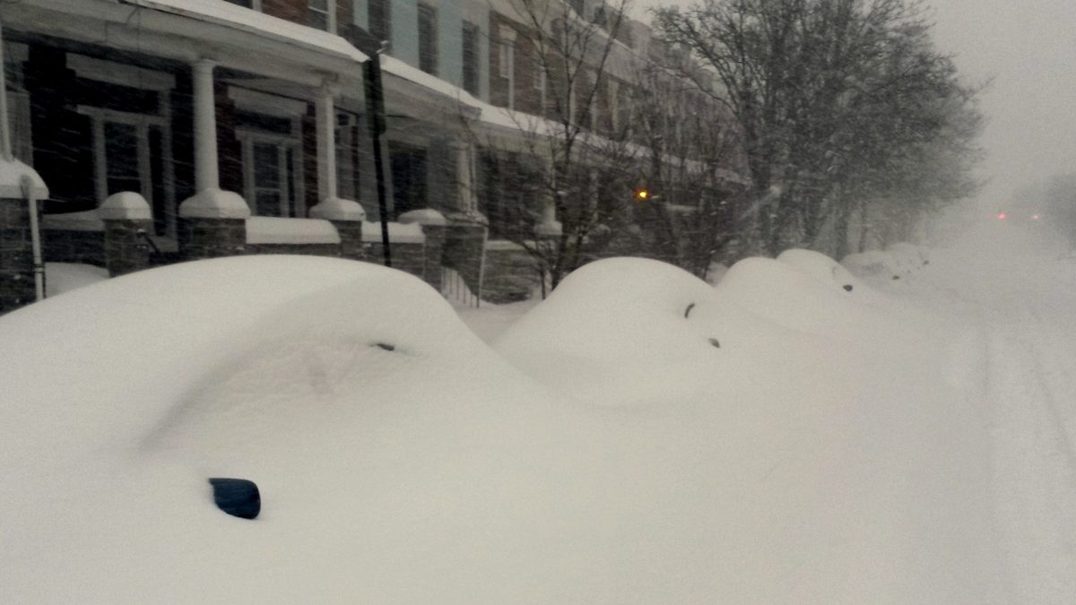 Cars buried to the roof in snow outside Baltimore rowhouses on Howard Street during the January 2016 blizzard, with snow still falling