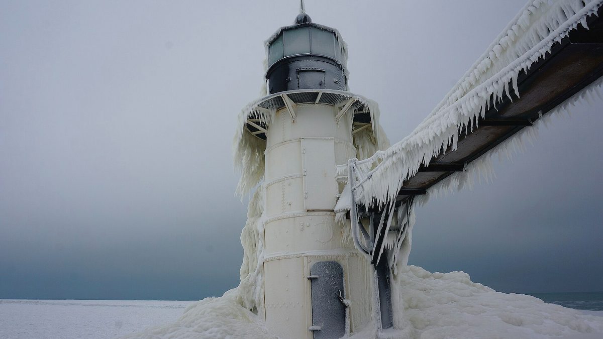 The St Joseph North Pier lighthouse on Lake Michigan encased in thick ice, with icicles hanging from the walkway beside it