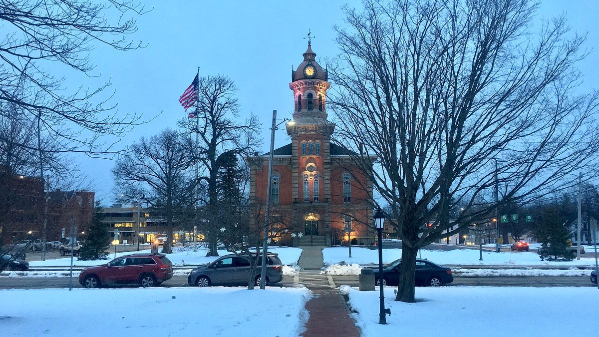 Snow covering Chardon Square at dusk with the lit Geauga County Courthouse clock tower behind it