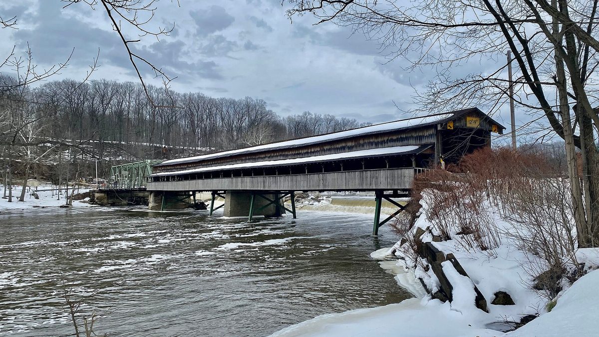 The Harpersfield Covered Bridge in Ashtabula County, Ohio under snow, with icicles hanging along its roof line above the Grand River