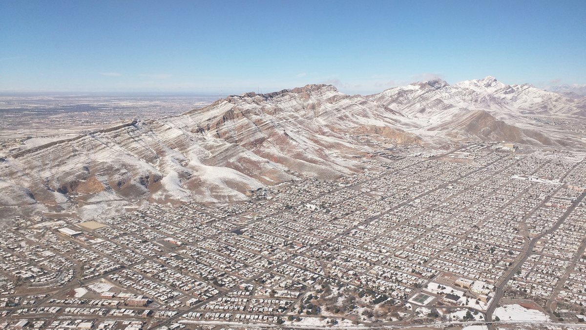 Aerial view of El Paso with the Franklin Mountains covered in snow rising behind the city grid