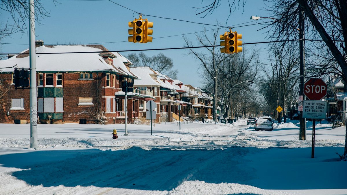 A residential street left unplowed after a snowstorm, with tyre ruts cut through the snow and cars buried at the kerb